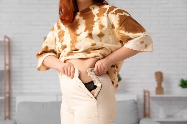 Image of woman trying to do her trousers up after pregnancy weight gain Sale